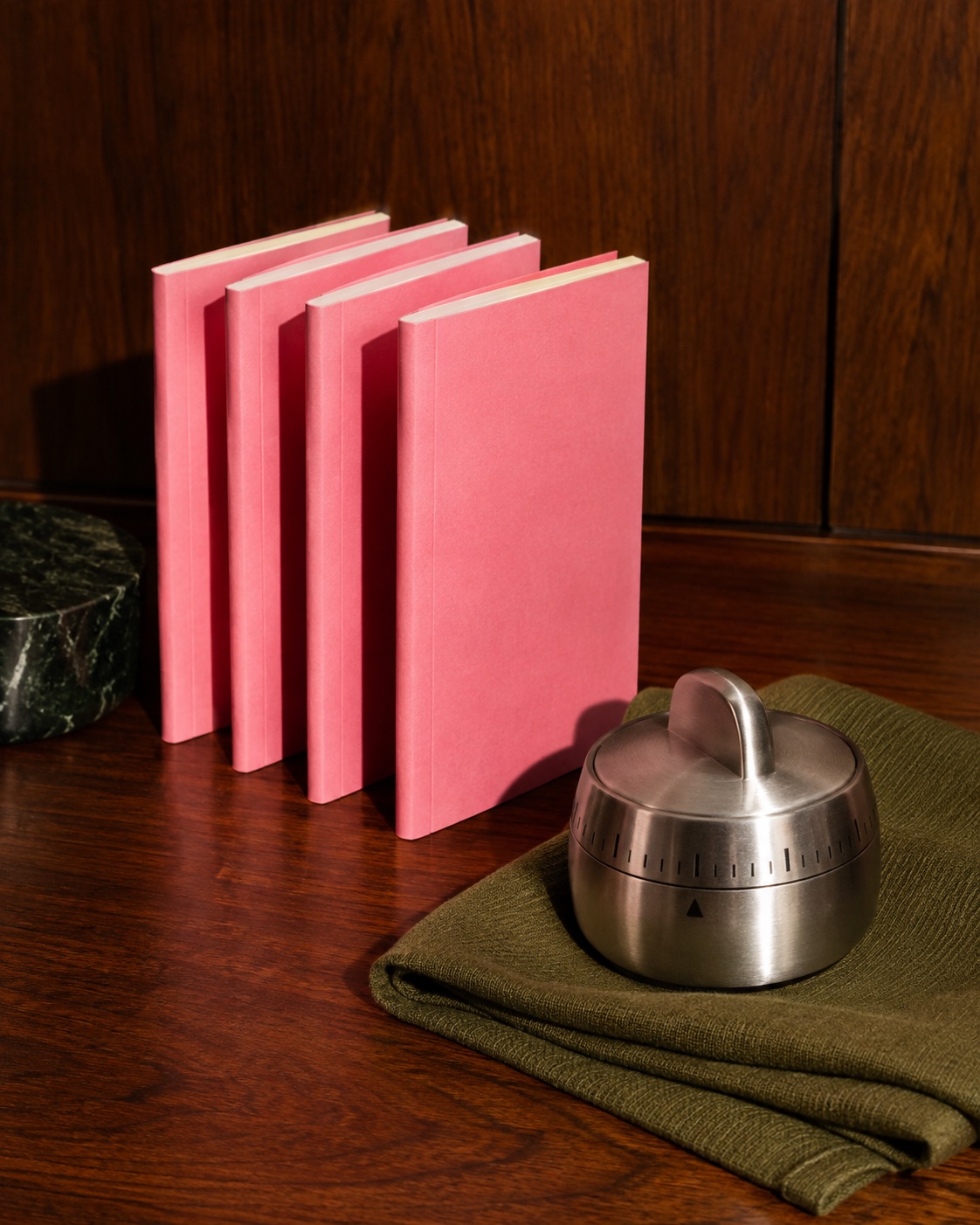 Pink notebooks and a silver timer on walnut wood